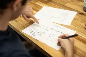 Tutor mengarahkan anak mengerjakan lembar kerja matematika di meja rumah